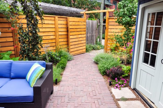 Contemporary with traditional elements, this beautiful small urban backyard garden features a seat wall, red brick paver herringbone pattern patio, natural stone steps and relaxing furniture.