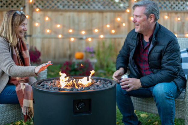 A husband and wife sitting next to a burning fire pit in their backyard
